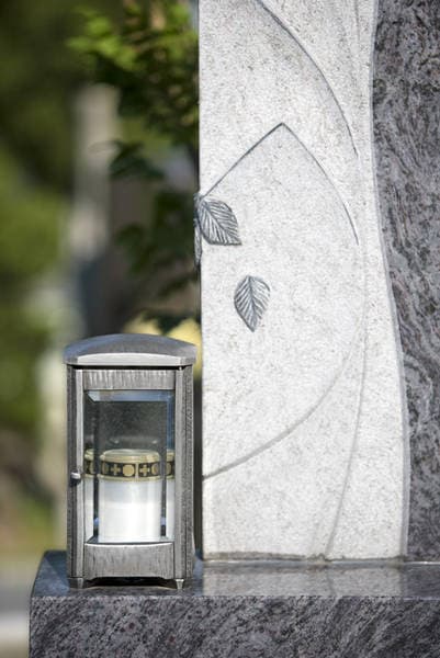 Detailaufnahme: Glas-Edelstahl-Laterne neben einem Granit-Grabstein mit Blattmotiv