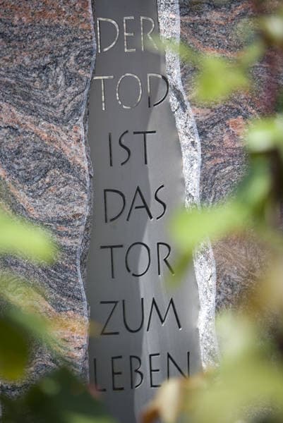 Vertikal eingravierte Inschrift „Der Tod ist das Tor zum Leben" auf mehrfarbigem Granit